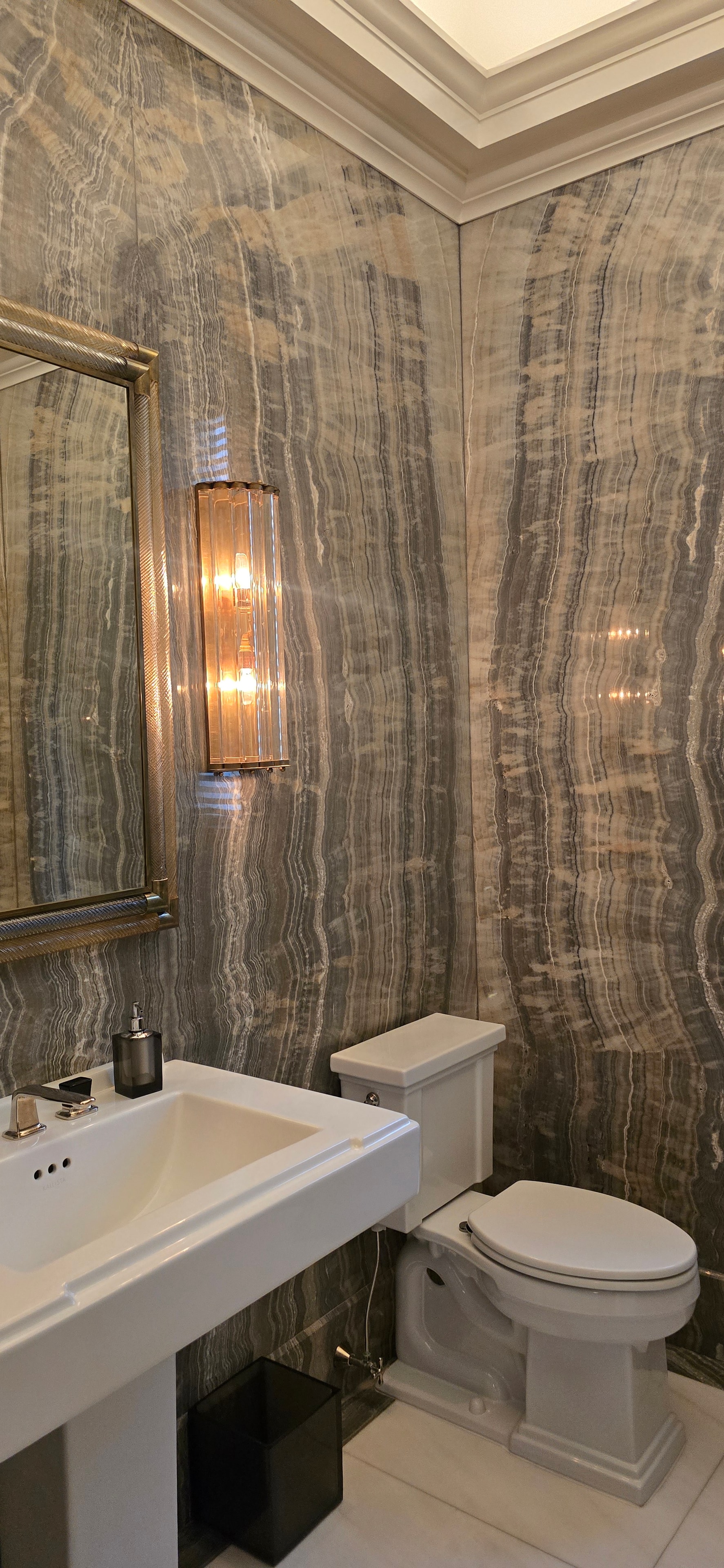 Dramatic onyx marble bathroom with gold-framed mirror and brass sconce