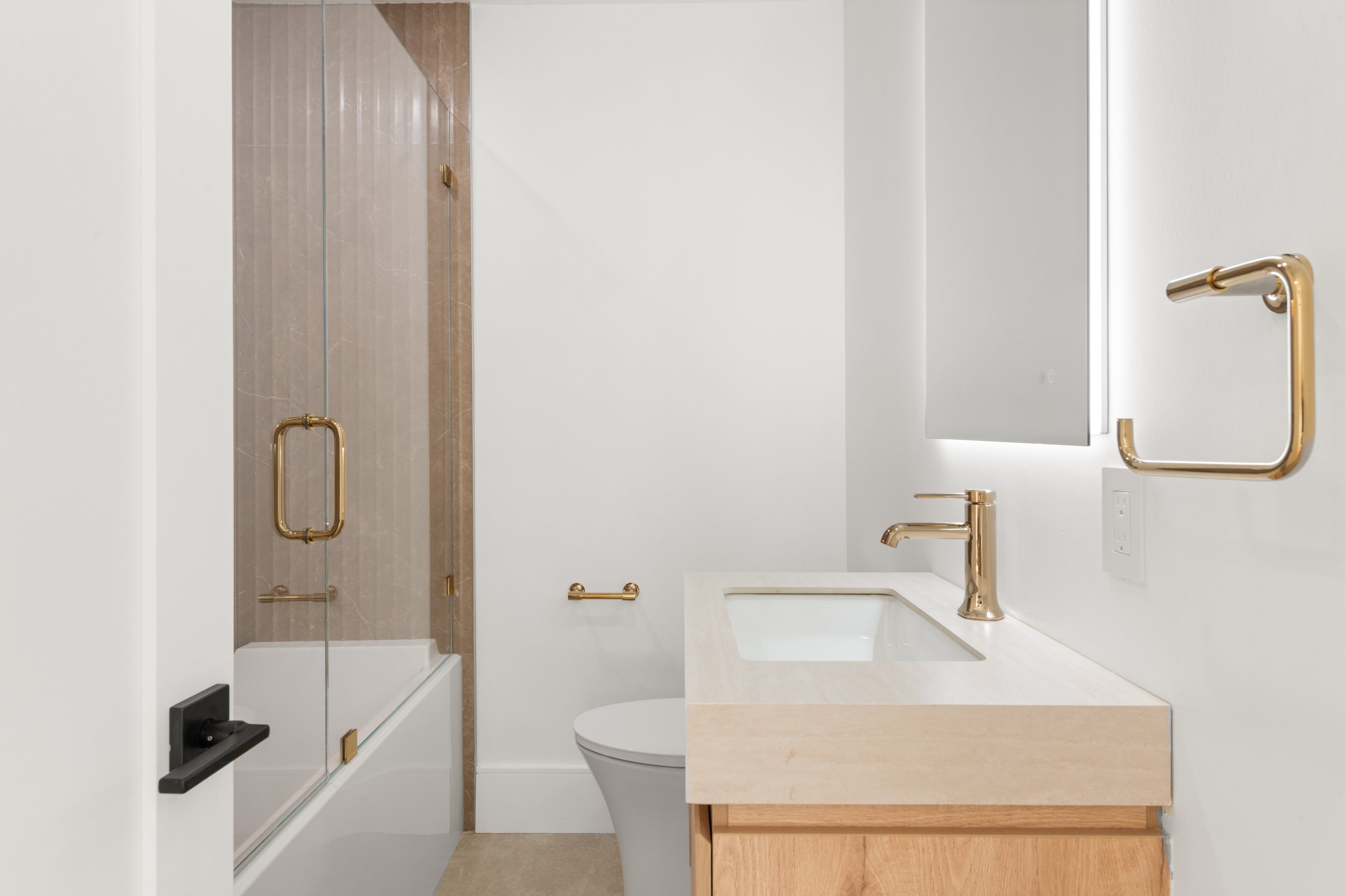 Modern bathroom with gold fixtures, glass shower enclosure, and wood vanity