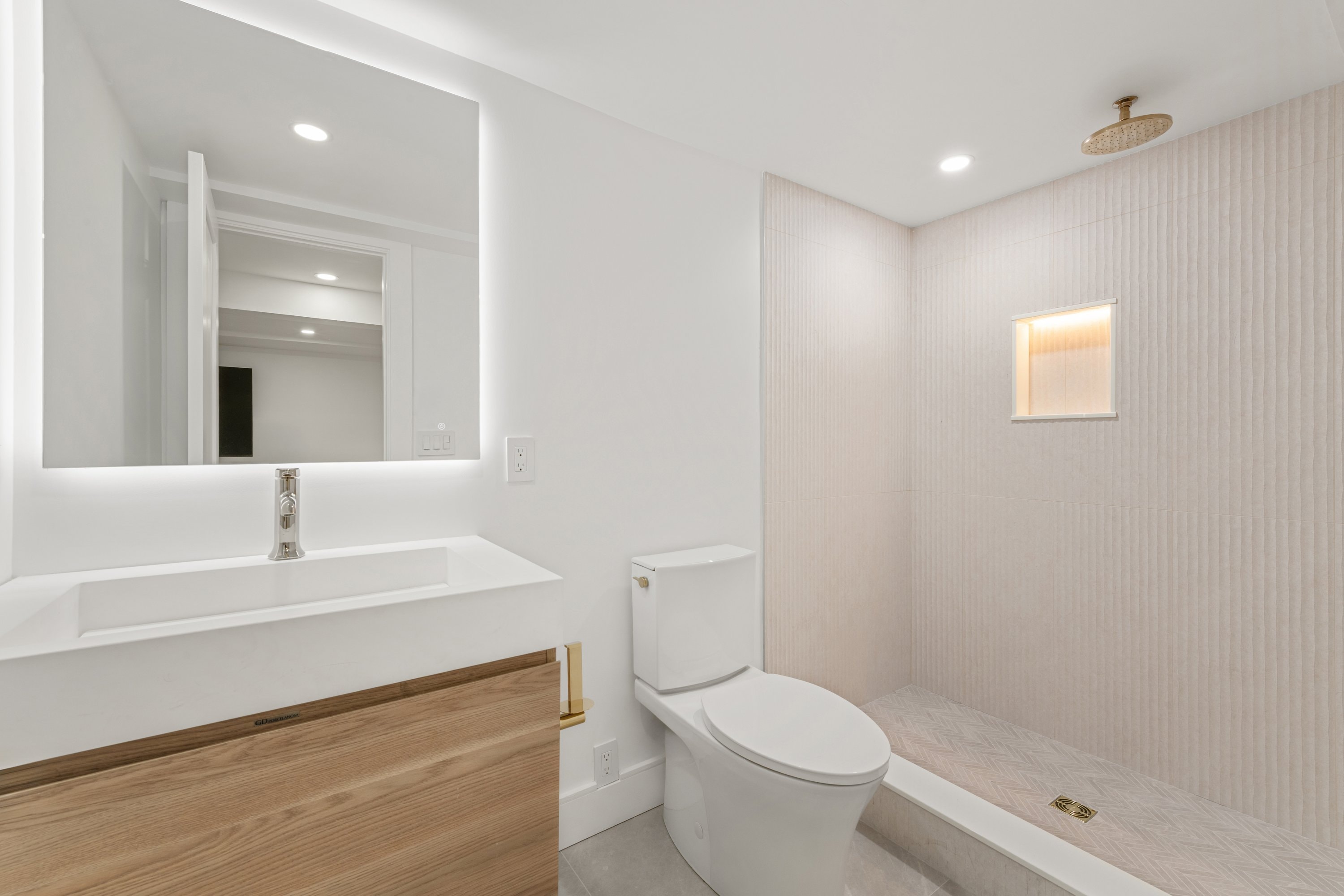 Bright bathroom renovation with backlit mirror, wood vanity, and walk-in shower