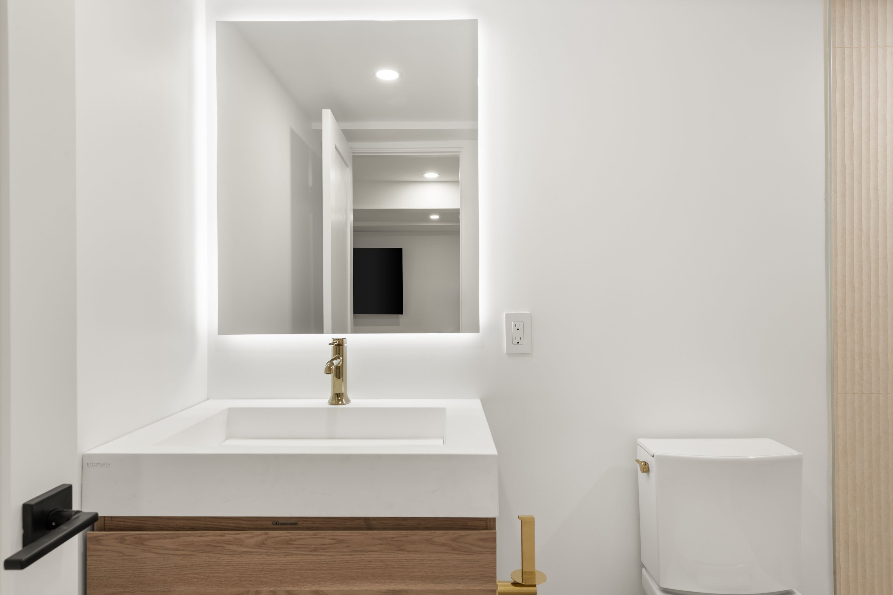 Clean modern bathroom with illuminated mirror, gold faucet, and floating vanity
